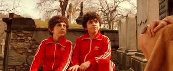 Movie still from “The Royal Tenenbaums” (2001), directed by Wes Anderson – Two young men in red tracksuits sitting next to each other in a cemetery; Medium shot, High angle