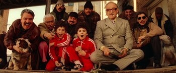 Movie still from “The Royal Tenenbaums” (2001), directed by Wes Anderson – A group of people sitting on the ground with a man sitting on the ground; Wide shot, Overhead angle