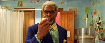Movie still from “The Royal Tenenbaums” (2001), directed by Wes Anderson – An older man wearing a bow tie eating a donut; Close Up shot, Low angle