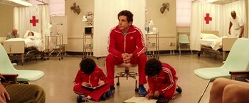 Movie still from “The Royal Tenenbaums” (2001), directed by Wes Anderson – A man sitting on top of a chair next to two other men; Medium shot, Low angle