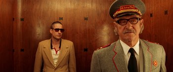 Movie still from “The Royal Tenenbaums” (2001), directed by Wes Anderson – A man in a suit standing next to another man in a suit; Medium shot, Low angle