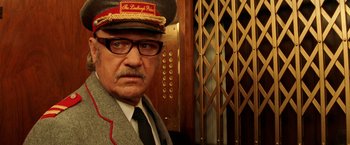 Movie still from “The Royal Tenenbaums” (2001), directed by Wes Anderson – An older man wearing a hat in front of an elevator; Close Up shot, Low angle