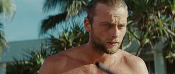 Movie still from “The Ruins” (2008), directed by Carter Smith – A person with a beard holding a tennis racquet; Close Up shot, Over the shoulder angle