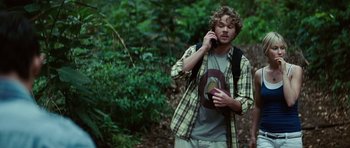 Movie still from “The Ruins” (2008), directed by Carter Smith – A young man talking on a cell phone while standing in the woods; Medium shot, Over the shoulder angle