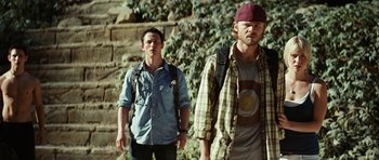 Movie still from “The Ruins” (2008), directed by Carter Smith – Two men standing next to each other near a stone wall; Medium shot, Low angle