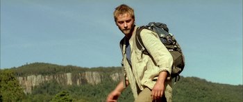 Movie still from “The Ruins” (2008), directed by Carter Smith – A man with a backpack walking on a trail; Medium shot, Low angle