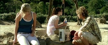 Movie still from “The Ruins” (2008), directed by Carter Smith – A woman sitting on a rock next to a radio; Medium shot, Over the shoulder angle