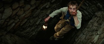 Movie still from “The Ruins” (2008), directed by Carter Smith – A man holding a light and a rope in his mouth; Medium shot, Overhead angle