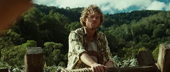 Movie still from “The Ruins” (2008), directed by Carter Smith – A man sitting on top of a rope in the middle of a forest; Medium shot, Low angle