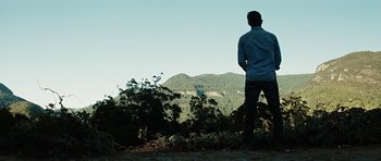 Movie still from “The Ruins” (2008), directed by Carter Smith – A man standing on top of a hill looking at a mountain; Extreme Wide shot, Low angle