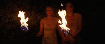 Movie still from “The Ruins” (2008), directed by Carter Smith – Two women are standing in front of a fire; Medium shot, Low angle