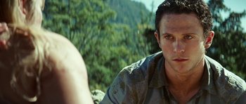 Movie still from “The Ruins” (2008), directed by Carter Smith – A person sitting on a rock near a forest; Close Up shot, Over the shoulder angle