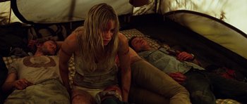 Movie still from “The Ruins” (2008), directed by Carter Smith – A woman sitting on a bed next to a man laying on the ground; Medium shot, High angle