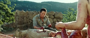 Movie still from “The Ruins” (2008), directed by Carter Smith – A man cutting a man's arm with a pair of scissors; Medium shot, High angle