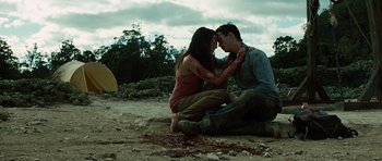 Movie still from “The Ruins” (2008), directed by Carter Smith – A man kneeling down next to a woman on the beach; Medium shot, High angle