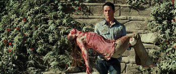 Movie still from “The Ruins” (2008), directed by Carter Smith – A man standing next to a woman with a dead body; Medium shot, Low angle