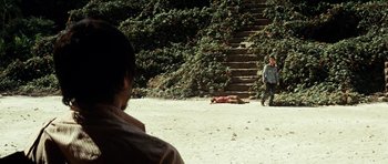 Movie still from “The Ruins” (2008), directed by Carter Smith – Two men standing on the beach looking at a dead body; Wide shot, Over the shoulder angle