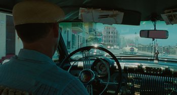 Movie still from “The Rum Diary” (2011), directed by Bruce Robinson – A man driving a car on a city street; Wide shot, Over the shoulder angle