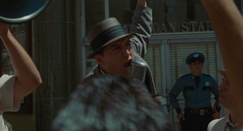Movie still from “The Rum Diary” (2011), directed by Bruce Robinson – A man with a hat and a microphone in front of a building; Medium shot, Low angle