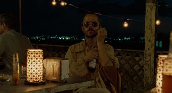 Movie still from “The Rum Diary” (2011), directed by Bruce Robinson – A man sitting on top of a wooden bench; Medium shot, Over the shoulder angle