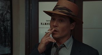 Movie still from “The Rum Diary” (2011), directed by Bruce Robinson – A man wearing a hat smoking a cigarette in a room; Close Up shot, High angle