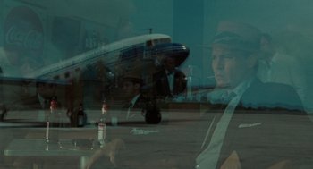Movie still from “The Rum Diary” (2011), directed by Bruce Robinson – A man sitting in front of an airplane on a runway; Medium shot, Over the shoulder angle
