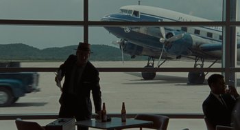 Movie still from “The Rum Diary” (2011), directed by Bruce Robinson – A man standing in front of an airplane with two beer bottles; Wide shot, Over the shoulder angle