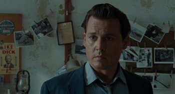 Movie still from “The Rum Diary” (2011), directed by Bruce Robinson – A man in a suit standing in front of a wall with pictures; Close Up shot, Over the shoulder angle