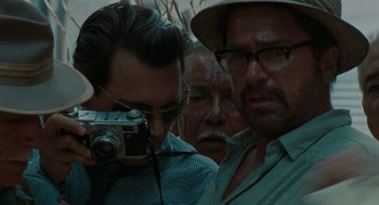 Movie still from “The Rum Diary” (2011), directed by Bruce Robinson – A man holding a camera in front of two other men; Close Up shot, Over the shoulder angle