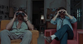 Movie still from “The Rum Diary” (2011), directed by Bruce Robinson – Two men sitting on a couch looking through binoculars; Wide shot, High angle