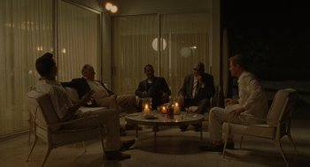 Movie still from “The Rum Diary” (2011), directed by Bruce Robinson – A group of men sitting around a table with candles on it; Wide shot, High angle