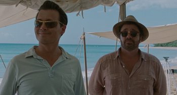 Movie still from “The Rum Diary” (2011), directed by Bruce Robinson – Two men standing next to each other on a beach; Medium shot, Over the shoulder angle