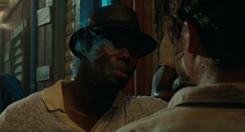 Movie still from “The Rum Diary” (2011), directed by Bruce Robinson – A man with a hat smoking a cigarette in front of another man; Close Up shot, Over the shoulder angle