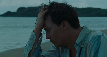 Movie still from “The Rum Diary” (2011), directed by Bruce Robinson – A man sitting on the beach holding his head with one hand; Close Up shot, High angle