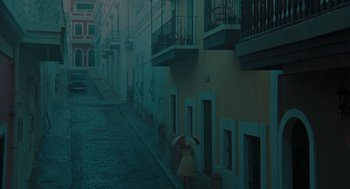 Movie still from “The Rum Diary” (2011), directed by Bruce Robinson – A woman with an umbrella walking down a street; Extreme Wide shot, High angle