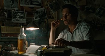 Movie still from “The Rum Diary” (2011), directed by Bruce Robinson – A man sitting at a table with a lit cigarette in his mouth; Medium shot, Low angle
