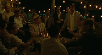 Movie still from “The Rum Diary” (2011), directed by Bruce Robinson – A group of men sitting around a table at a party; Wide shot, High angle
