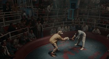 Movie still from “The Rum Diary” (2011), directed by Bruce Robinson – Two men are fighting in an arena while people watch from the stands; Wide shot, High angle