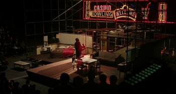 Movie still from “The Salesman” (2016), directed by Asghar Farhadi – A man sitting at a table in front of a neon sign; Extreme Wide shot, High angle