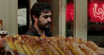 Movie still from “The Salesman” (2016), directed by Asghar Farhadi – A man standing in front of a table of food; Close Up shot, Over the shoulder angle