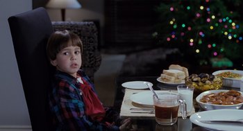 Movie still from “The Santa Clause” (1994), directed by John Pasquin – A boy sitting at a table with a plate of food on it; Medium shot, Over the shoulder angle