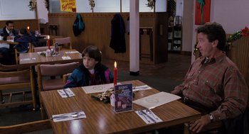 Movie still from “The Santa Clause” (1994), directed by John Pasquin – A child sitting at a table with a book on it; Medium shot, Over the shoulder angle