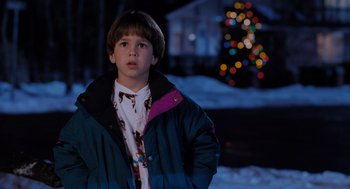 Movie still from “The Santa Clause” (1994), directed by John Pasquin – A young boy in a blue jacket standing in the snow; Medium shot, High angle