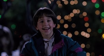 Movie still from “The Santa Clause” (1994), directed by John Pasquin – A young boy smiling for the camera in front of a christmas tree; Close Up shot, Low angle