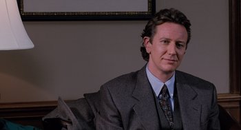 Movie still from “The Santa Clause” (1994), directed by John Pasquin – A man wearing a suit and tie sitting in a chair; Close Up shot, Over the shoulder angle