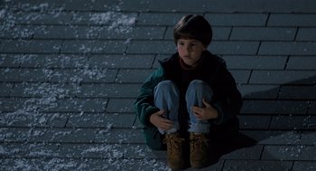 Movie still from “The Santa Clause” (1994), directed by John Pasquin – A young boy sitting on the ground in the snow; Wide shot, High angle