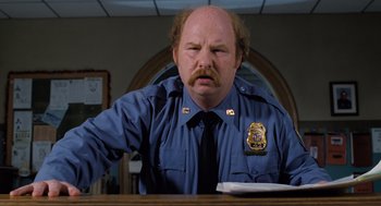 Movie still from “The Santa Clause” (1994), directed by John Pasquin – A police officer sitting at a table with a plate in front of him; Close Up shot, Low angle