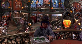 Movie still from “The Santa Clause 2” (2002), directed by Michael Lembeck – A person sitting at a table with a gift box; Wide shot, High angle