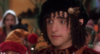 Movie still from “The Santa Clause 2” (2002), directed by Michael Lembeck – A young man wearing a green hat and a red and gold outfit; Close Up shot, Over the shoulder angle