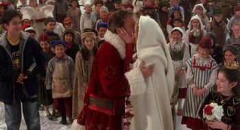 Movie still from “The Santa Clause 2” (2002), directed by Michael Lembeck – A man and a woman dressed as santa claus kissing in front of a crowd of children; Medium shot, Over the shoulder angle